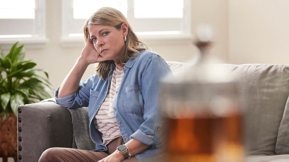 [Image:] A sister sitting on her sofa, staring across the room at a bottle of alcohol.