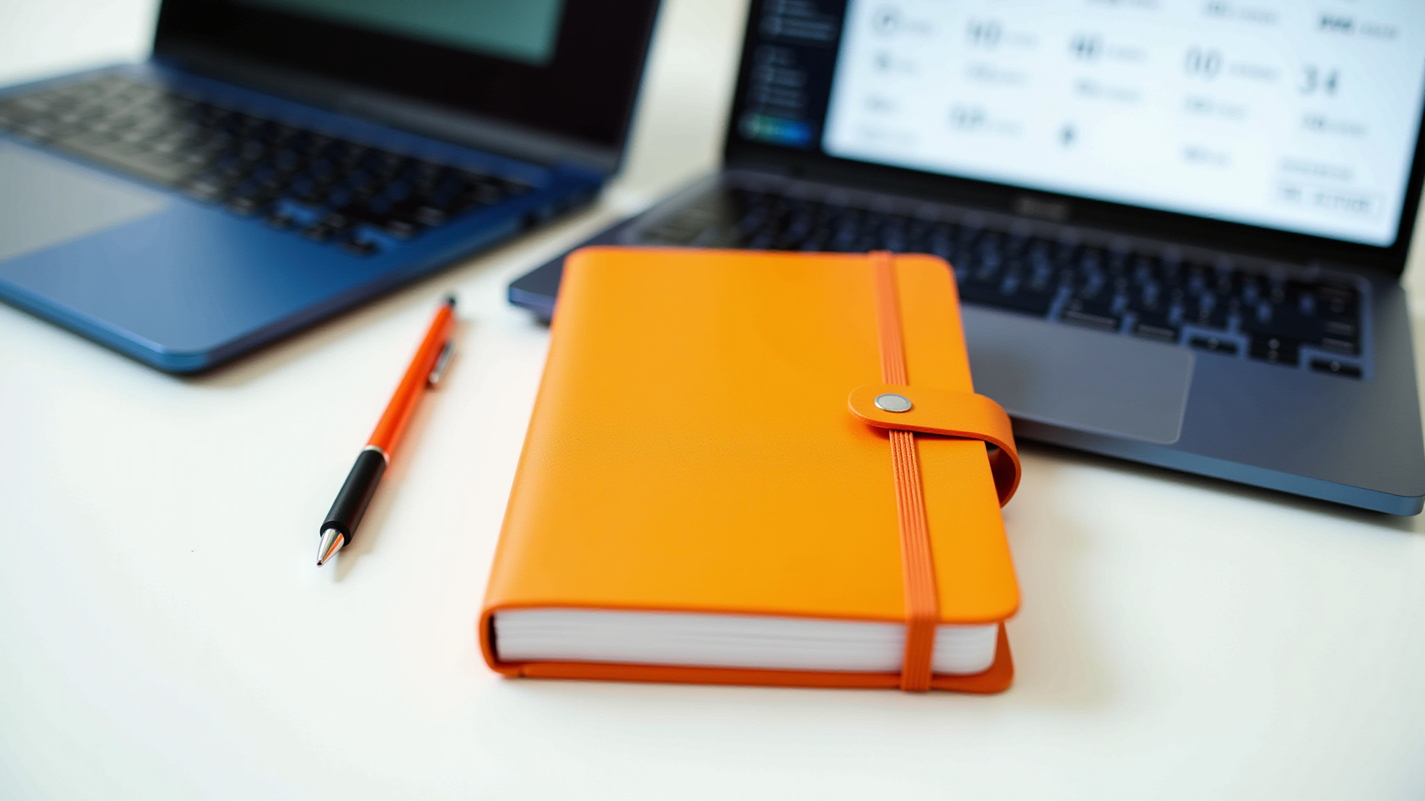 Orange notebook and pen with laptops