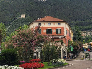 Colorful apartment building with flower beds on a curving street beneath steep forested mountains; APARTMENTS sign visible.