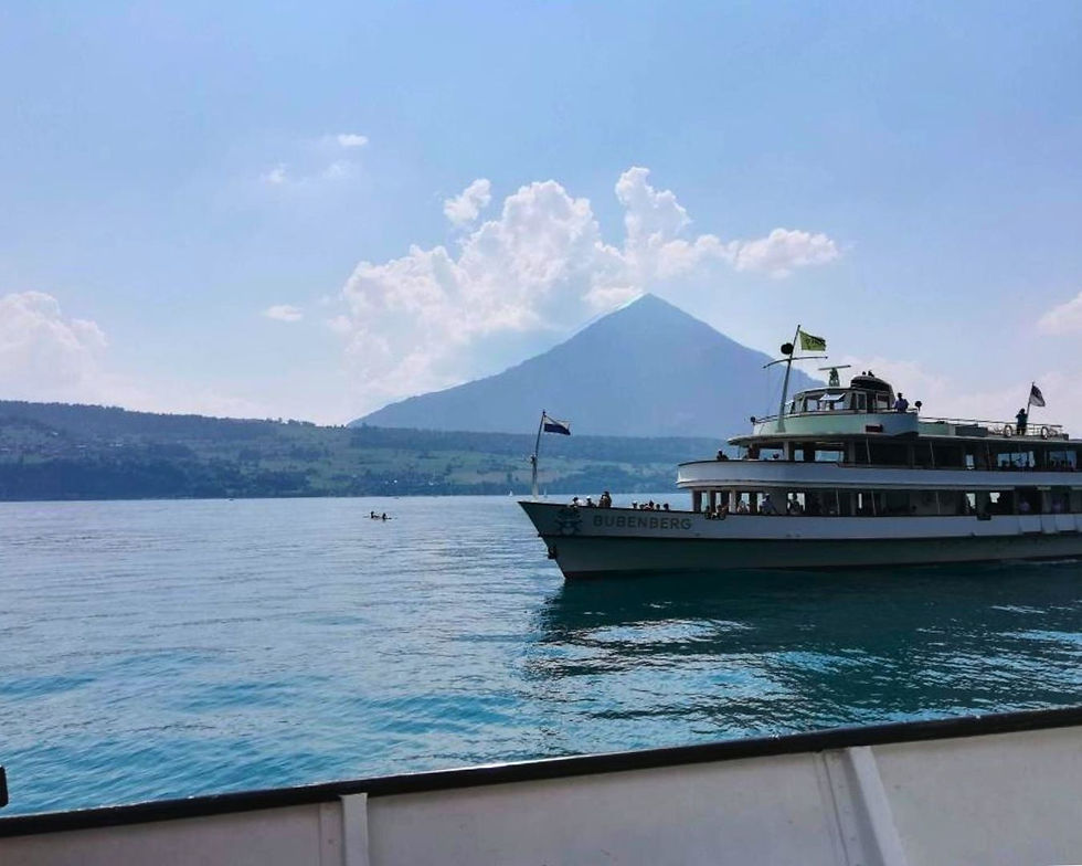Ferry named "Bubenberg" on a calm lake with a mountain and fluffy clouds in the background. Peaceful, clear blue sky and water.
