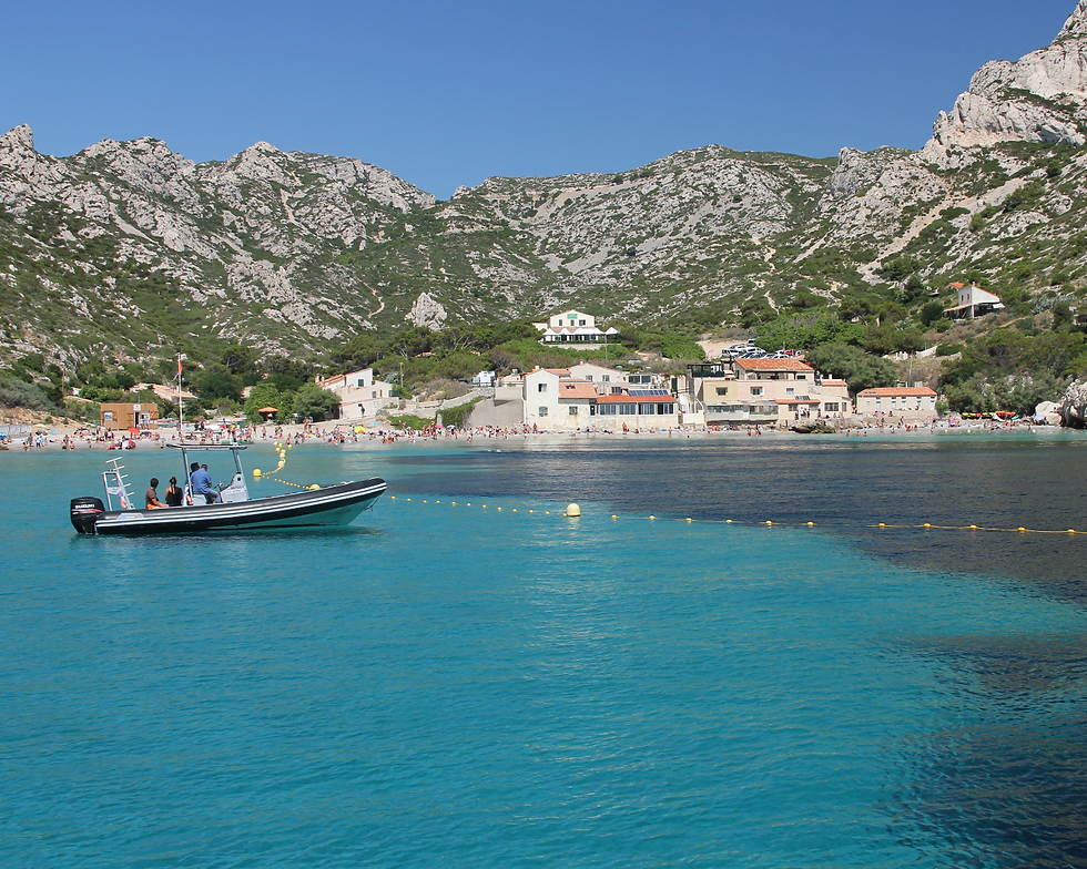 A boat the the sea with the village and mountains in the background