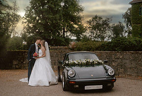 Brautpaar küsst sich im Sonnenuntergang neben ihrem Porsche Oldtimer, fotografiert von Raluca Wassmus im Wasserschloss Unsleben