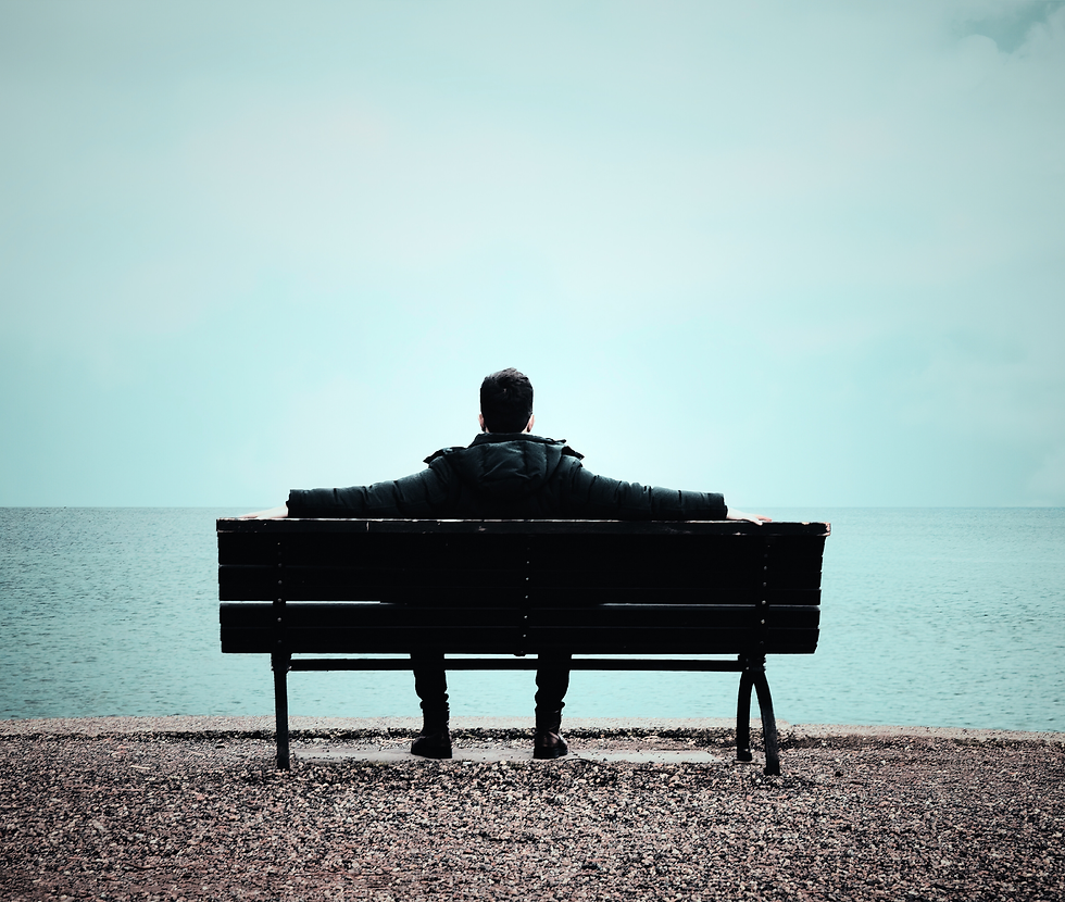 Person sitting on bench alone watching water in landscape. This represents how after relational captivity and coercive control, one slowly starts coming back into present time. This is the return to self.