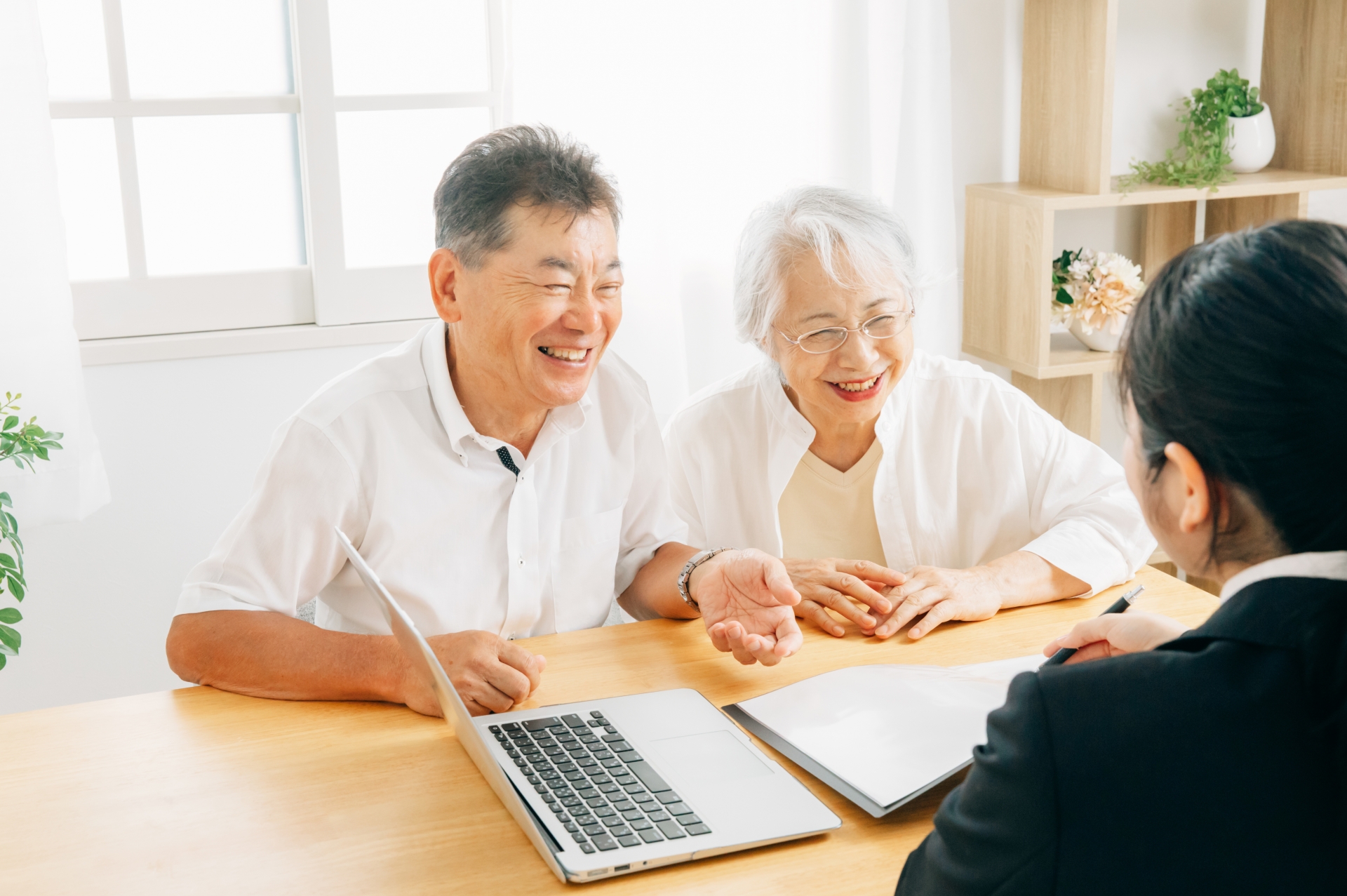 老人ホームの入居相談でパソコン画面を見ながら話すシニア夫婦と専門スタッフ