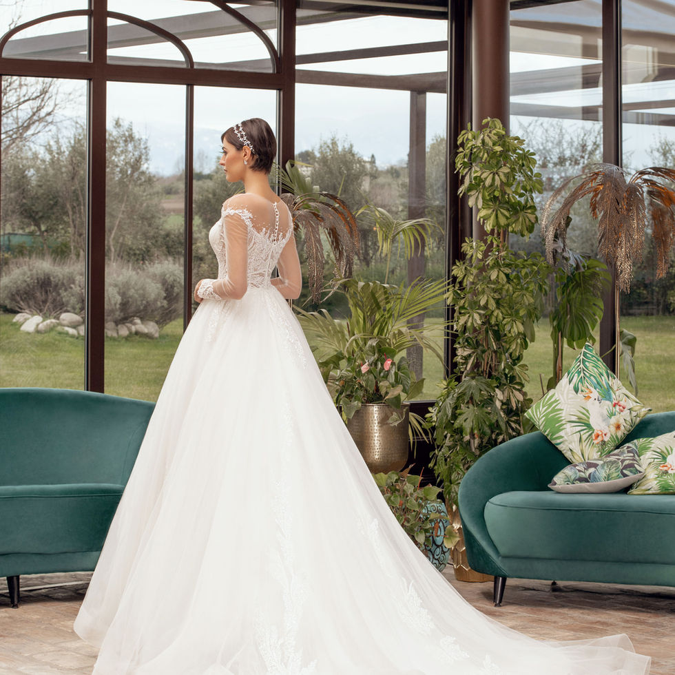 Sposa in abito bianco guarda fuori, contesto naturale; Sposami Atelier.