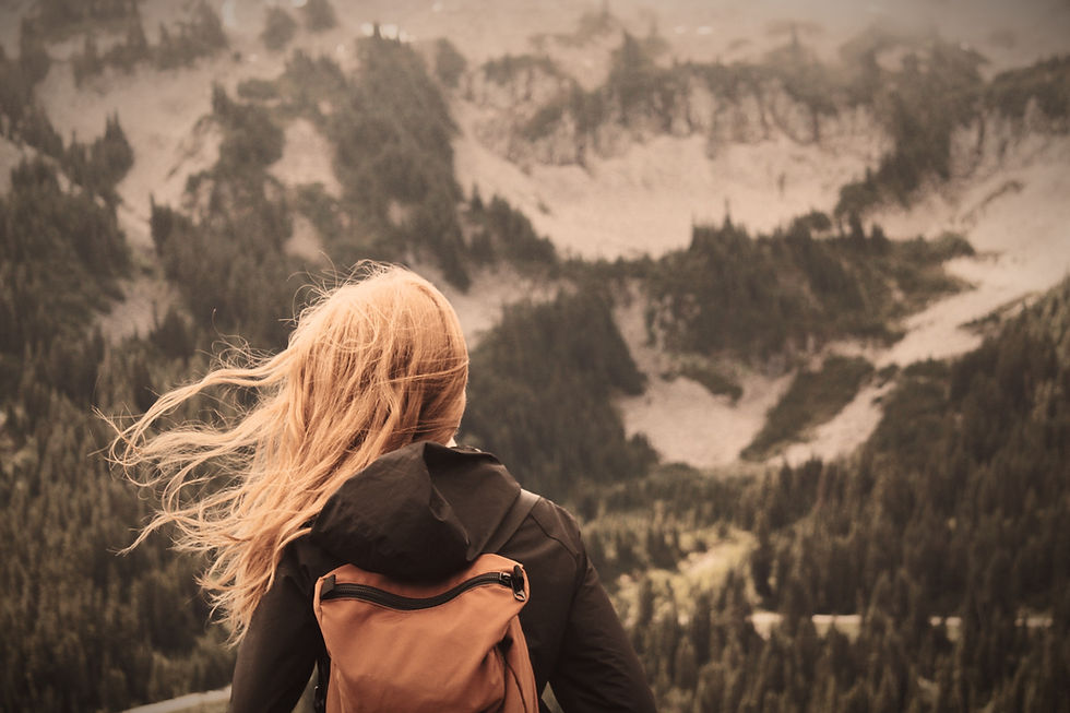 We see a young girl from behind with a backack, facing snowing mountainous terrain