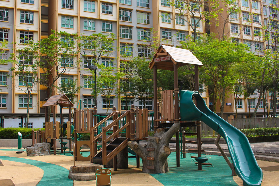 Playground with green slide and wooden structures labeled "Kids Only" in front of high-rise buildings, surrounded by trees.