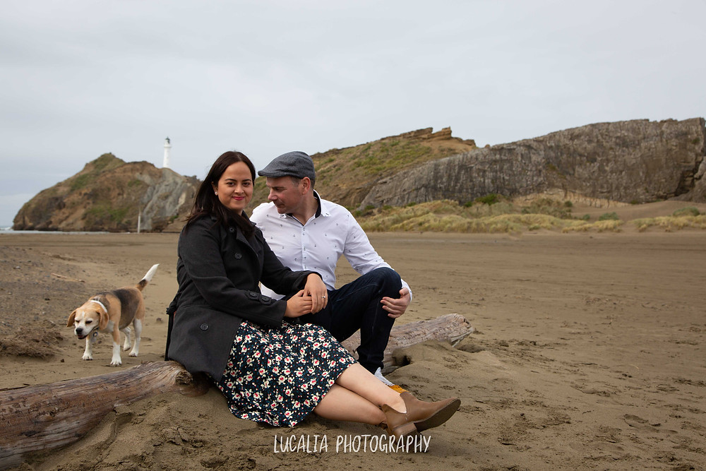 engaged couple sitting on the beach with their dog at Castlepoint lighthouse, Lucalia Photography Wairarapa wedding photographer