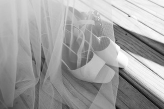 natural black and white photo of bridal wedding shoes and dress tulle outside on a deck