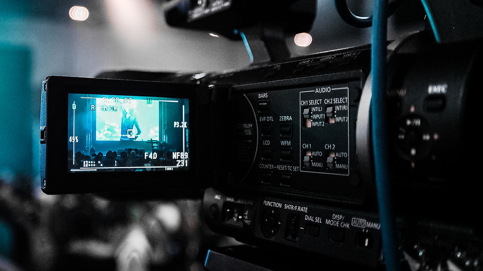 Close-up of a video camera display showing a blurred crowd and stage in blue tones. The camera's controls and buttons are visible.