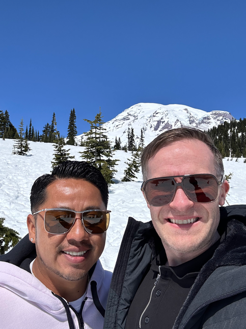 Two men smiling in sunglasses with a snowy mountain