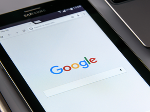 Close-up of a electronic tablet displaying the Google homepage with search bar. The screen is active and colourful in an office setting.