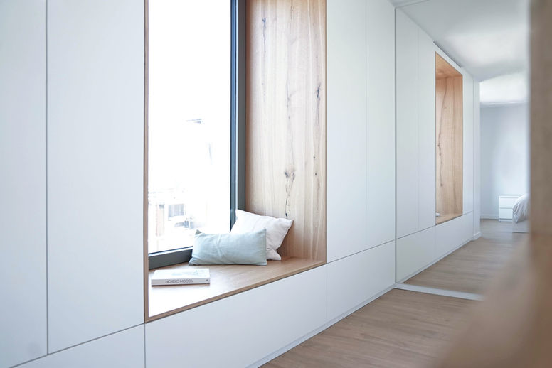 Ankleidezimmer in weiß und Naturholz mit integrierter Sitzbank am Fenster und großer Spiegelwand.