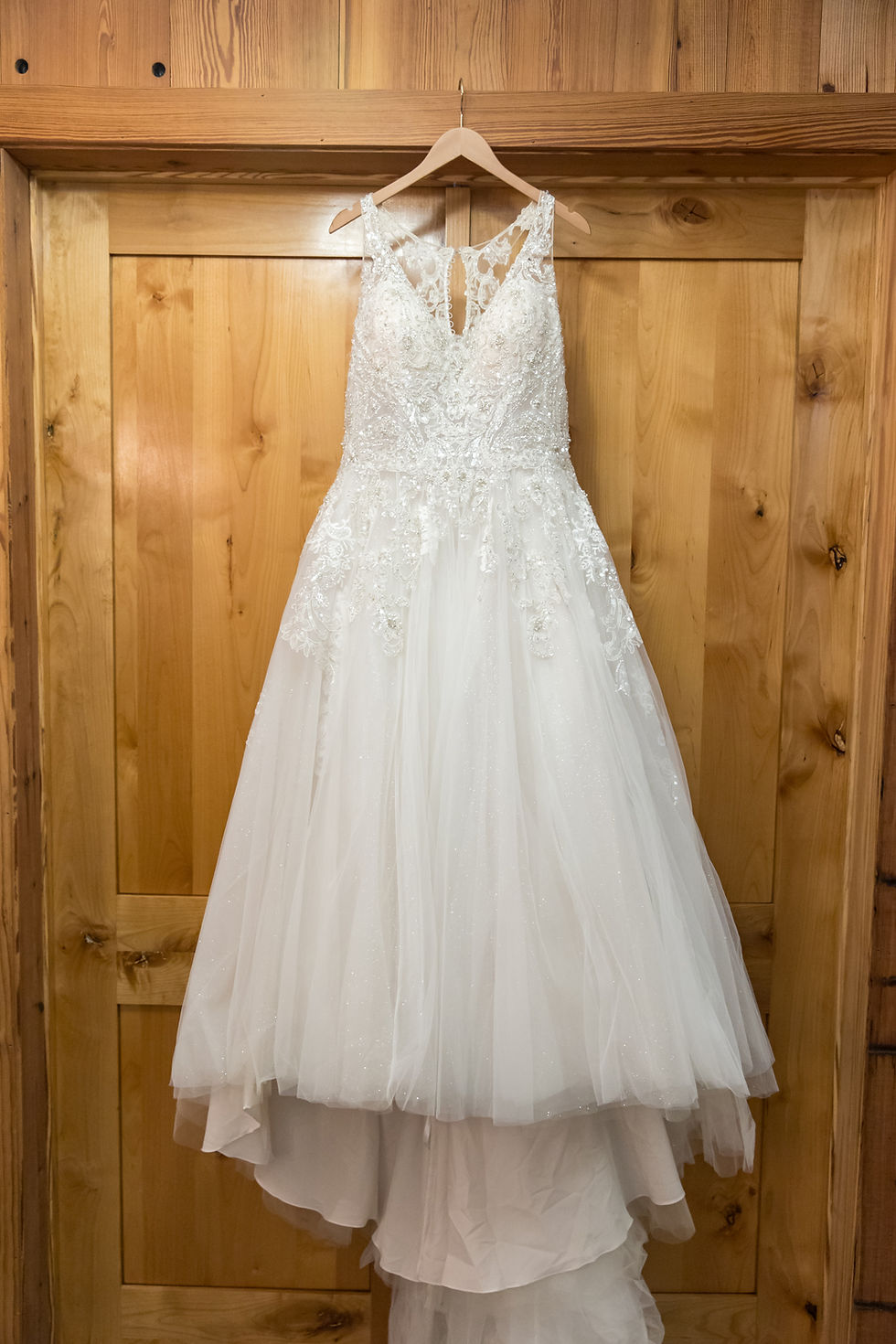 Wedding dress hanging on wood hanger.