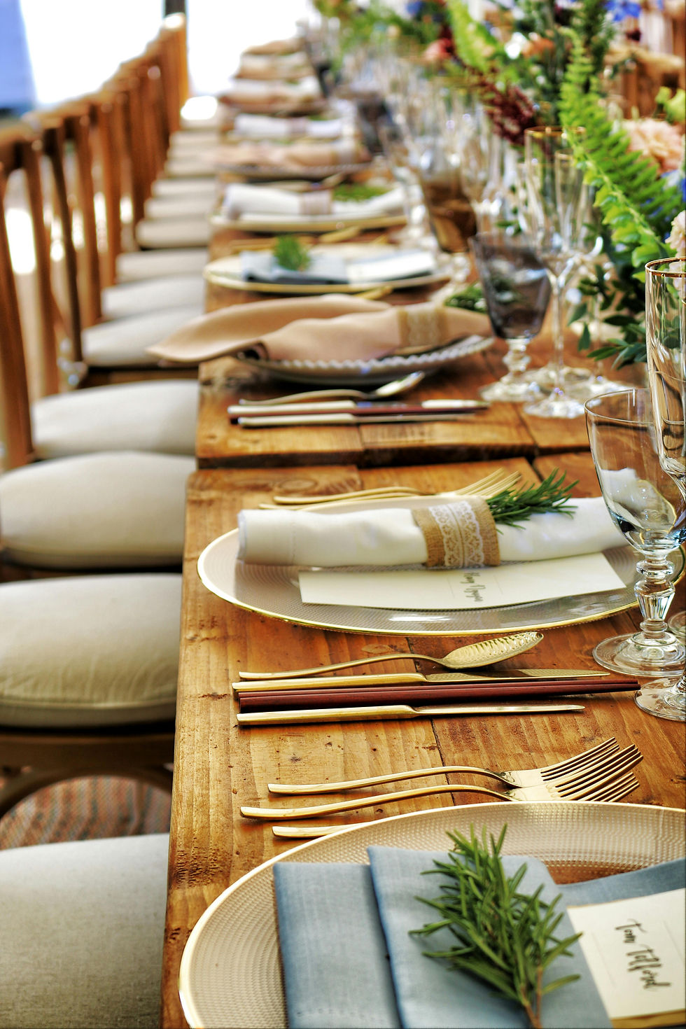 Wedding table setting with rolled napkin, charger, and greenery details.