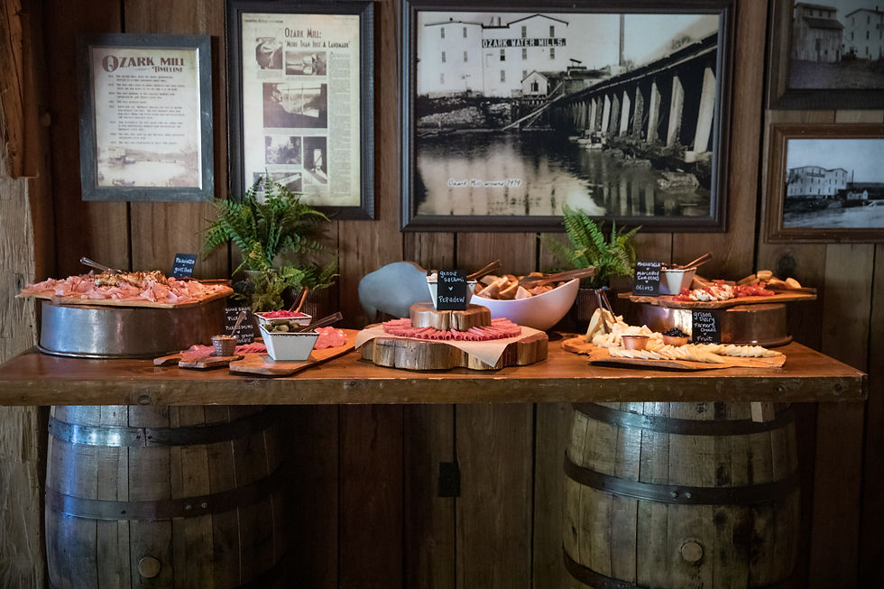 Rustic charcuterie buffet on wooden barrels with labeled meats, cheeses and olives.