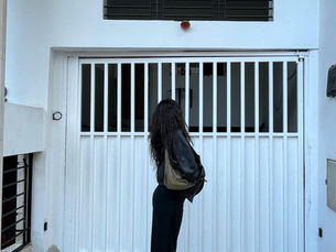 Women standing infant of garage, wearing black pants and leather jacket looking away from the camera