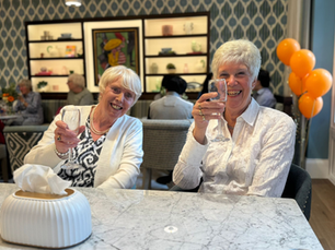 two attractive ladies smiling sat at a table in an aylesbury nursing home celebrating and drinking champagne.