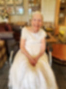 Beautiful older lady in a care home sat smiling at the camera once again wearing her wedding dress.