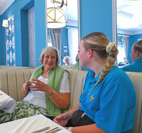 Team member and care home resident laughing with one another while sat at dining table