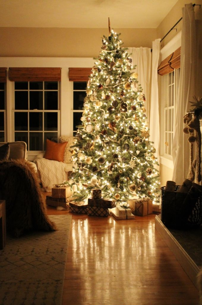 Lit Christmas tree with ornaments in a cozy room, surrounded by wrapped gifts on wooden floor. Warm, festive ambiance with soft lighting.