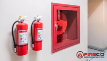 Two red fire extinguishers with ABC labels on a wall beside a red fire hose cabinet. Fire safety logo and text on the right.