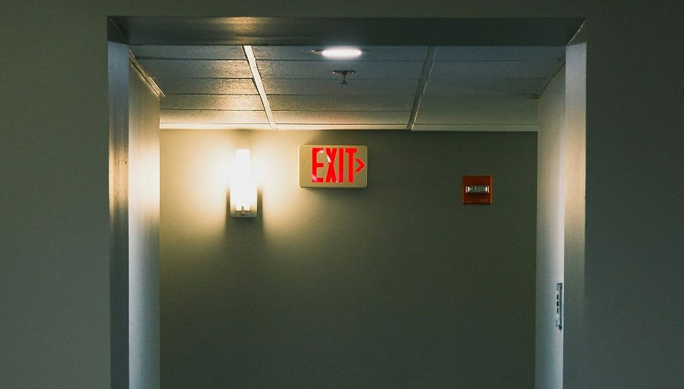 Hallway with a lit "EXIT" sign in red, wall-mounted light, and gray walls, creating a calming yet purposeful atmosphere.