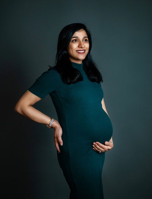 Maternity mom seated on the floor in simple gown with hands on belly – minimalistic indoor maternity portrait by Camories