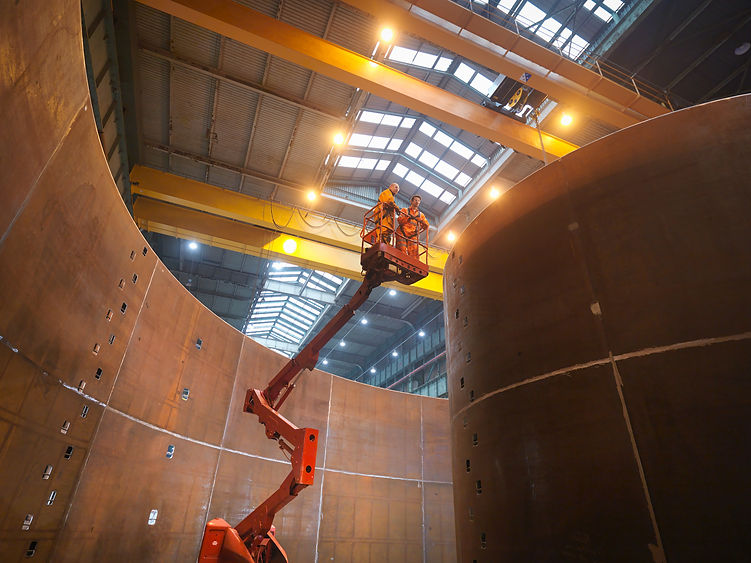 Two men in a cherry picker access tower on an industrial site