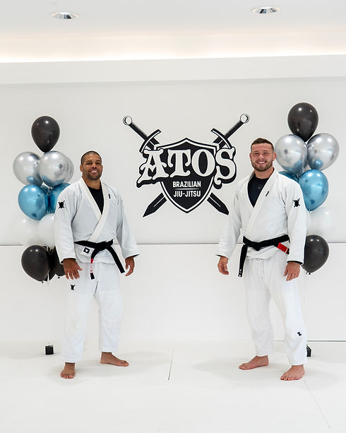 Two jiu jitsu coaches with Atos logo in background