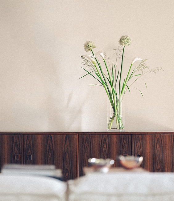 Vase mit hohen, dünnen Blumen auf einem dunklen Holzsideboard vor einer hellen Wand