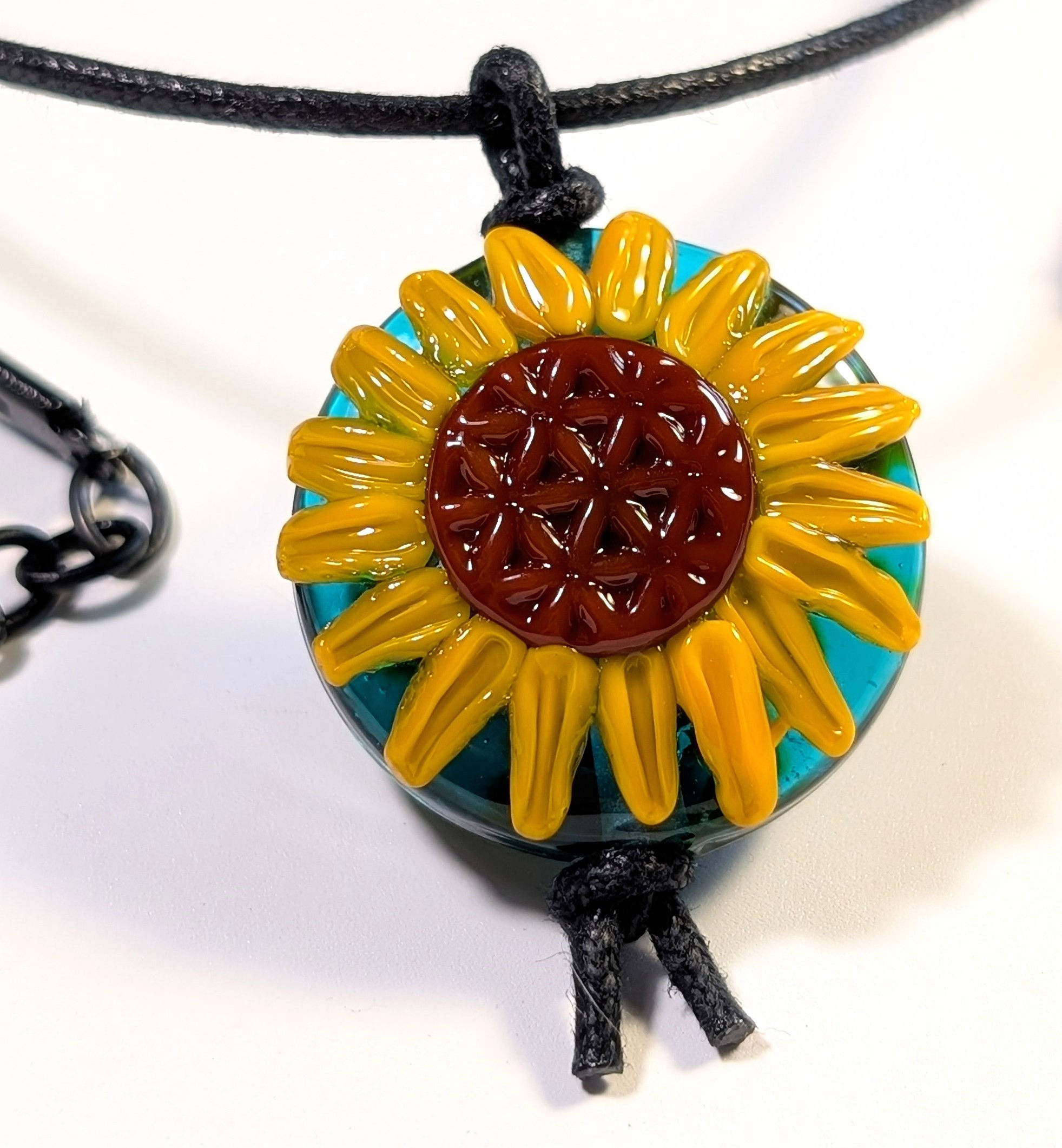 teal lampwork pendant with a flower of life centered sunflower on black cord close up pendant view