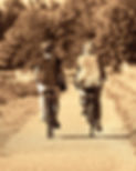 2 women riding bikes side by side down a path
