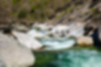 Rocky river with clear turquoise water flowing through boulders. Wooden bridge and trees in lush, green forest backdrop. Tranquil scene. Hell Canyon Jerte Valley, Spain
