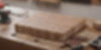 A beautifully crafted wooden cutting board is prominently displayed on a workbench, featuring the inspirational inscription "Life's too short, do what makes you happy!". The surrounding woodworking tools and sawdust reinforce the theme of creation and personal fulfillment through craft.