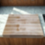 A thick, light-colored maple wooden cutting board with a prominent grain is the central focus,