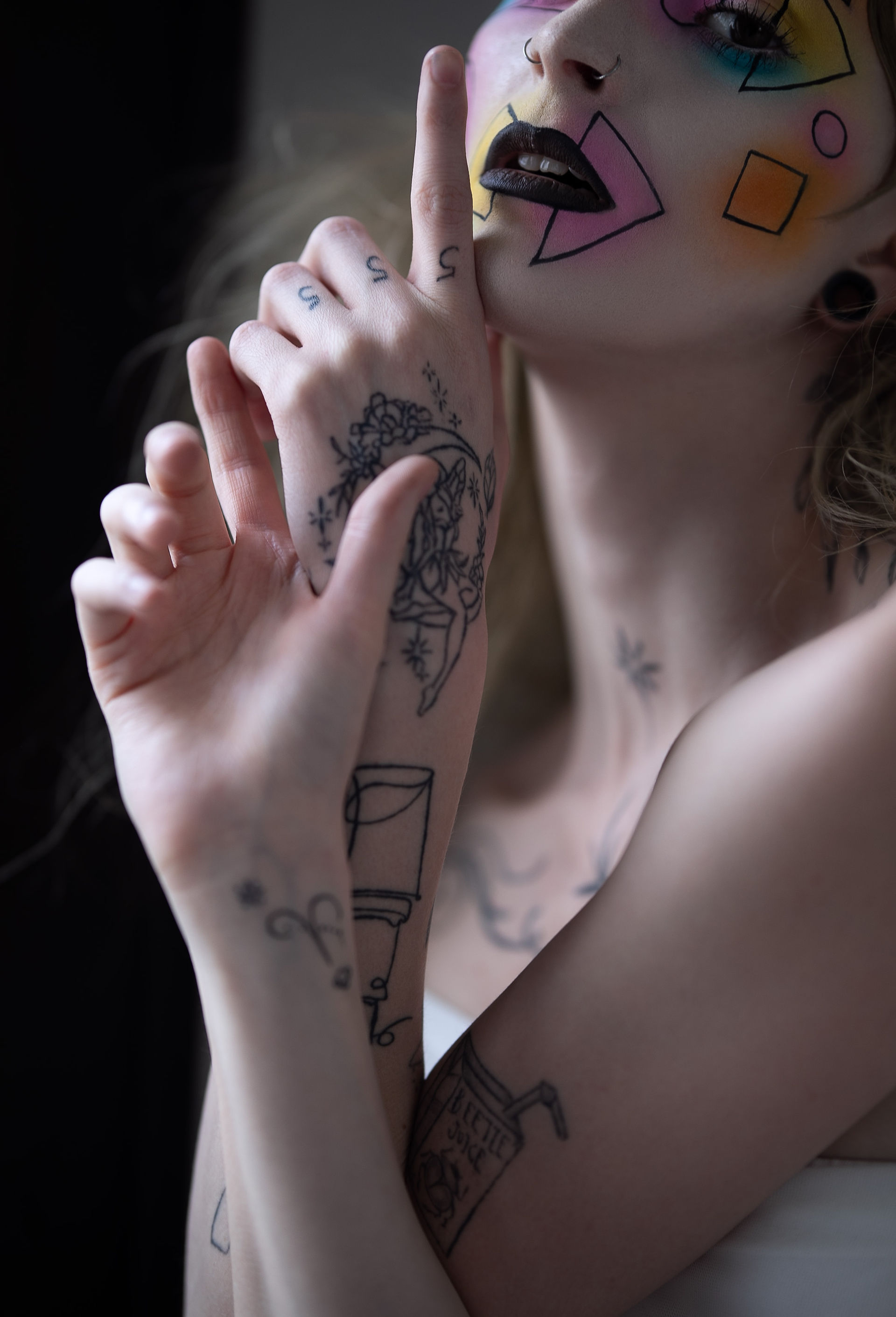 Close-up portrait of Jade posing with tattooed hands framing her colorful geometric makeup.