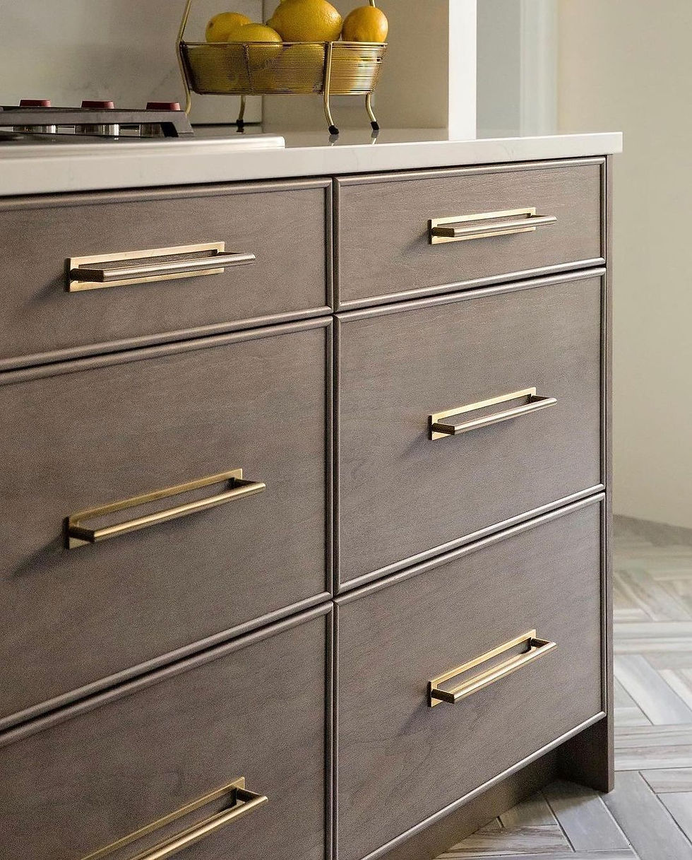 Wooden kitchen drawers with gold handles, topped with a white counter and a basket of lemons. Geometric patterned floor.