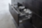 A photograph of a set of kitchen cabinets with one drawer open. The cabinets are of a very dark wood.