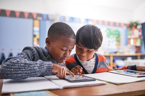 Two young boys reading a tablet in a classroom