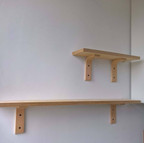 Two rows of wooden scaffold shelves, attached to the wall with simple brackets. The top shelf is half the length of the bottom shelf