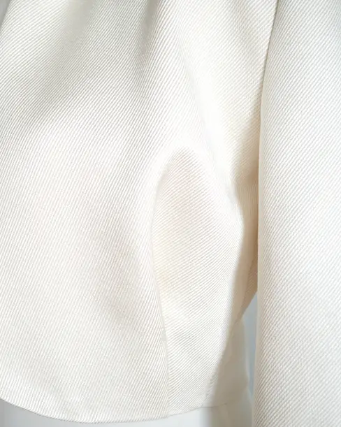 Detalle en primer plano de la textura de la seda rústica color marfil, tejido con sutil brillo y relieve diagonal