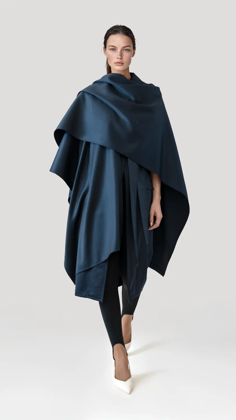 Modelo luciendo chaleco con capa envolvente azul noche de lana virgen, silueta fluida y elegante.