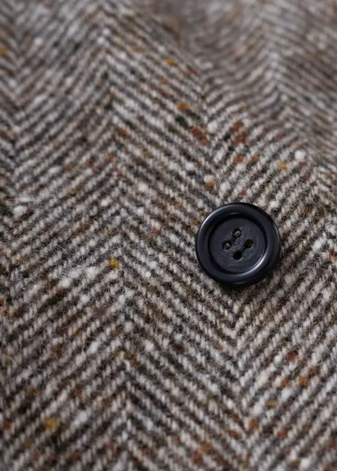 Detalle del tejido espiga en lana marrón con botón negro, textura cálida y acabado artesanal.