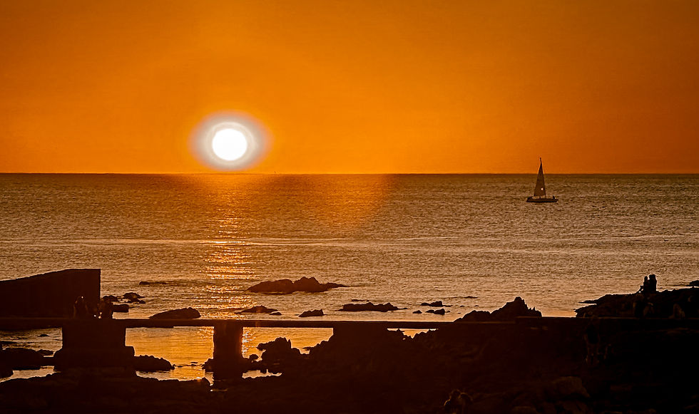 pôr do sol no mar, pedras e um barco ao horizonte.