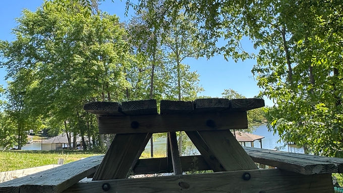 Picnic table by calm water under trees representing peace in troubled waters and standing in Christ (Romans 5 teaching)