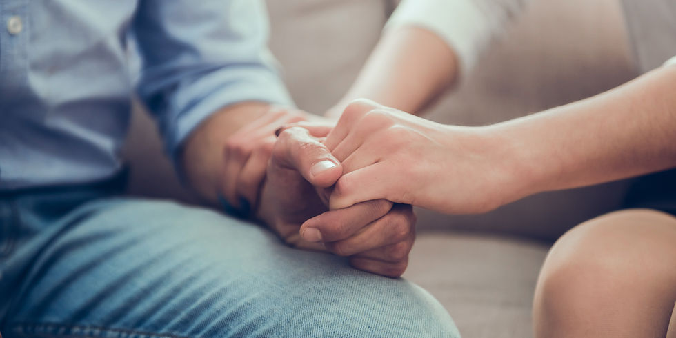 Two people hold hands, conveying comfort. One wears a blue shirt and jeans. Background is a soft, blurred interior, evoking a calm mood.