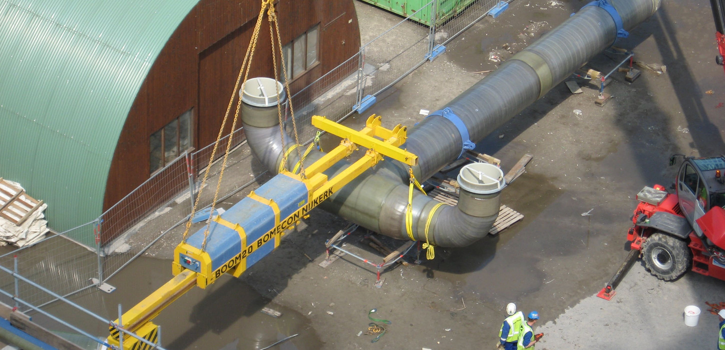 Draufsicht: Ein Kran hebt ein massives Y-förmiges Rohr auf einem Industriegelände an.