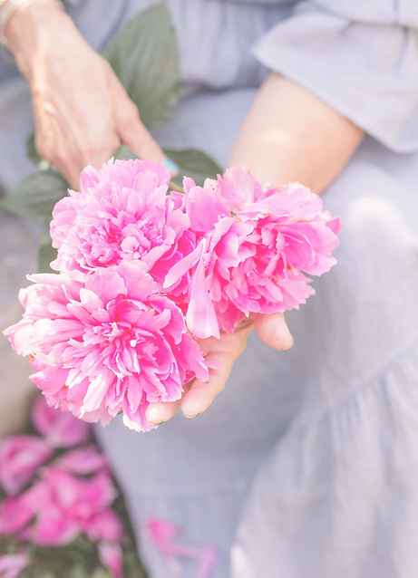 A woman in a gray dress holding bright pink peonies.