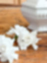 Gardenias on a rustic wooden table beside a white ceramic vase.